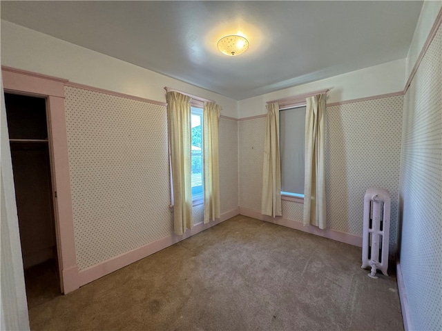 unfurnished bedroom with a closet, radiator heating unit, and carpet flooring