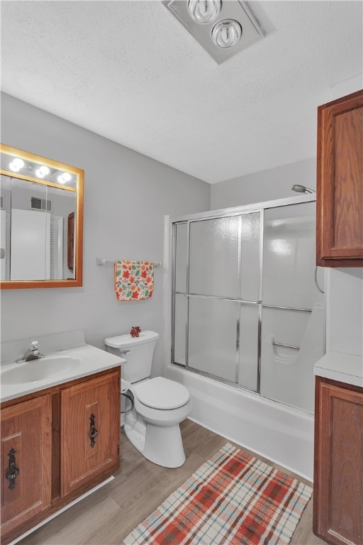 full bathroom with hardwood / wood-style floors, combined bath / shower with glass door, a textured ceiling, toilet, and vanity