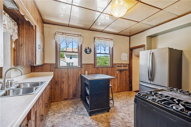 kitchen with stainless steel fridge, sink, wooden walls, and range with gas cooktop