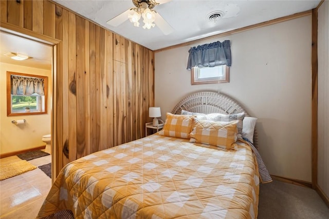 bedroom with visible vents, baseboards, ceiling fan, ensuite bath, and wood walls