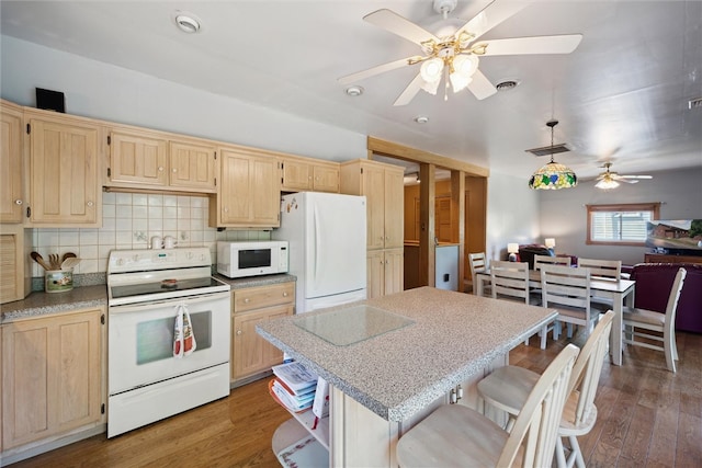 kitchen featuring ceiling fan, white appliances, dark hardwood / wood-style floors, light brown cabinetry, and a breakfast bar area