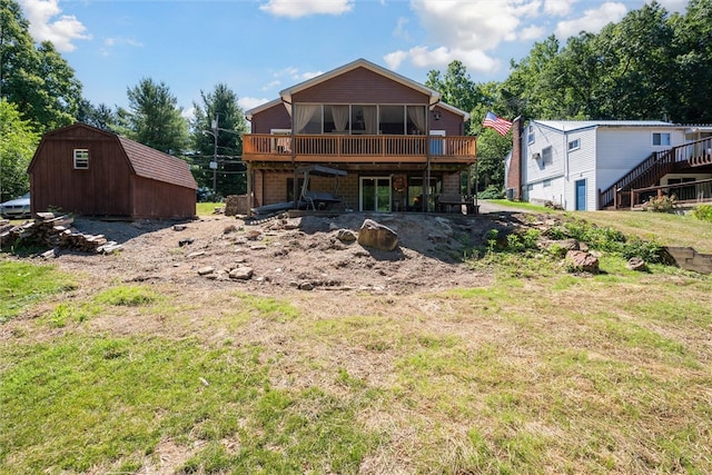 rear view of property featuring a wooden deck, a lawn, a storage shed, a sunroom, and an outbuilding