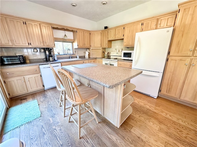 kitchen with white appliances, a kitchen island, light brown cabinetry, a sink, and light wood-type flooring