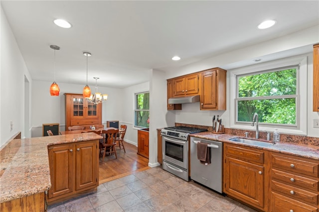 kitchen with appliances with stainless steel finishes, decorative light fixtures, sink, kitchen peninsula, and light stone countertops