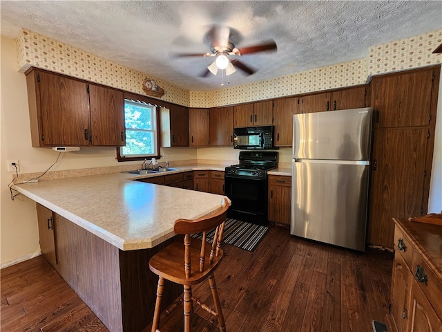 kitchen with a textured ceiling, dark hardwood / wood-style floors, kitchen peninsula, and black appliances