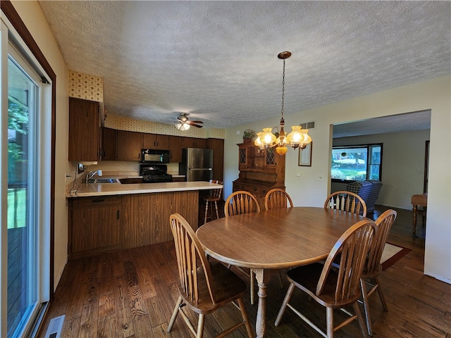 dining area featuring dark wood-type flooring, sink, ceiling fan with notable chandelier, and a textured ceiling