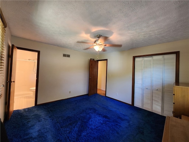 unfurnished bedroom with a textured ceiling, carpet floors, a closet, ceiling fan, and ensuite bathroom