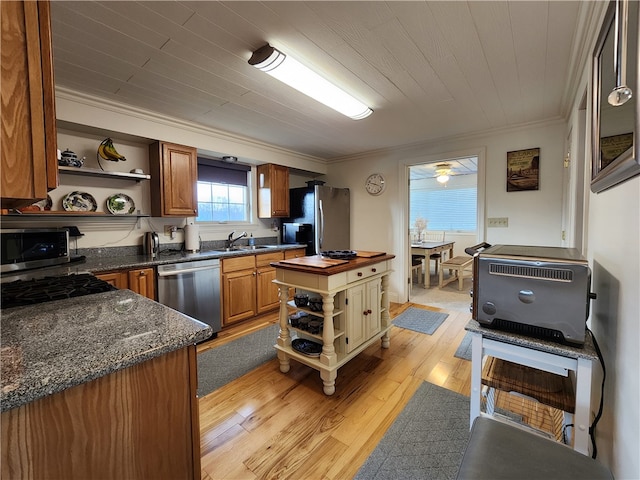 kitchen with appliances with stainless steel finishes, dark stone counters, sink, light hardwood / wood-style floors, and crown molding