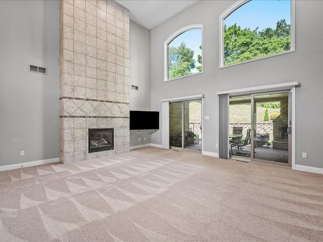 unfurnished living room with a towering ceiling, light carpet, and a tile fireplace