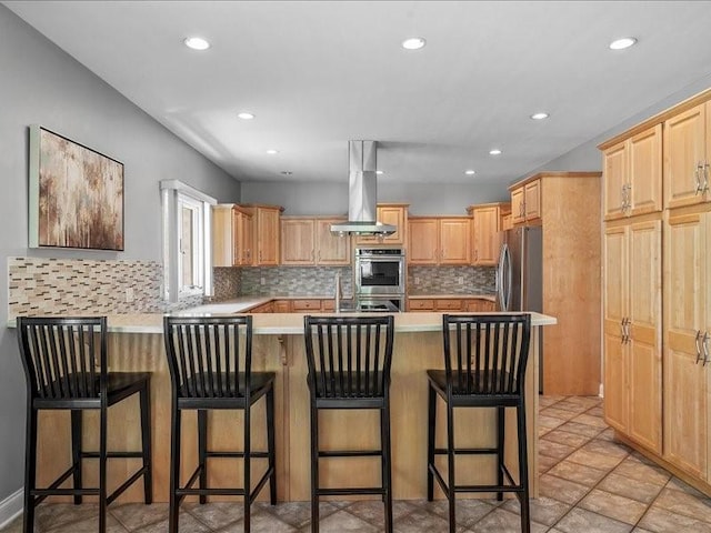 kitchen featuring light brown cabinetry, appliances with stainless steel finishes, island range hood, a kitchen bar, and kitchen peninsula