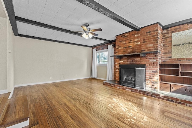 unfurnished living room with ceiling fan, beam ceiling, wood-type flooring, and a brick fireplace