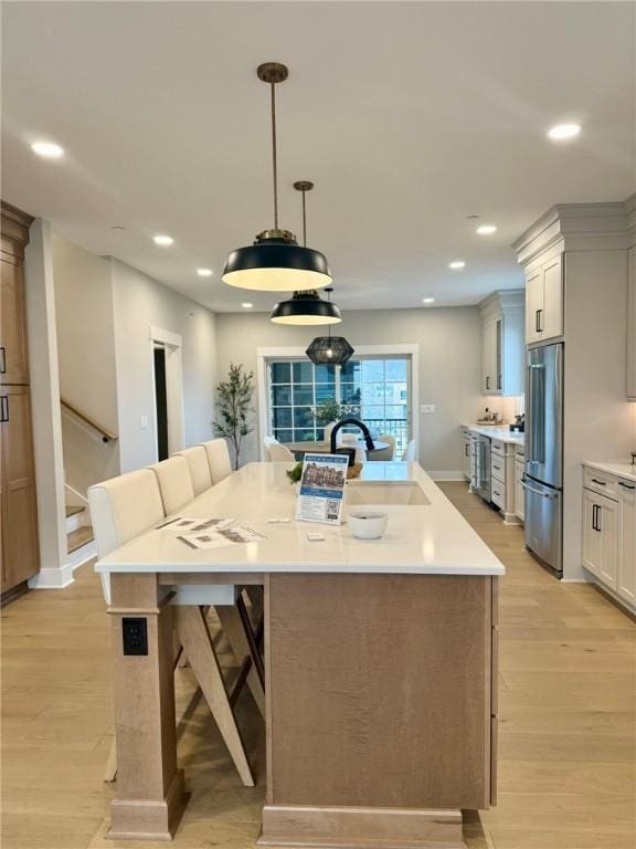 kitchen featuring a kitchen breakfast bar, sink, a large island with sink, pendant lighting, and stainless steel refrigerator