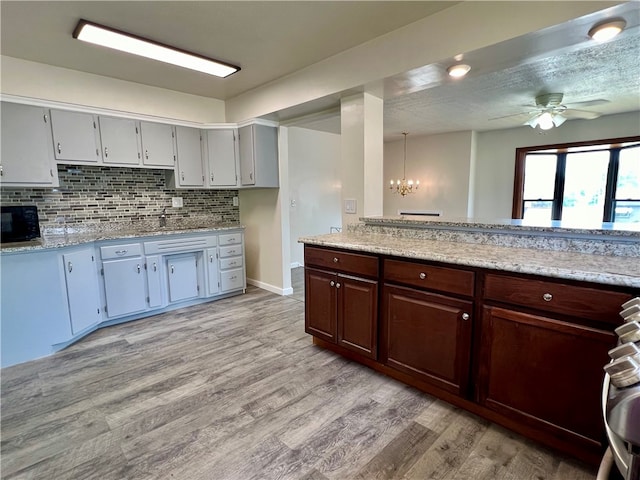 kitchen with dark brown cabinetry, decorative backsplash, light wood-type flooring, and ceiling fan with notable chandelier