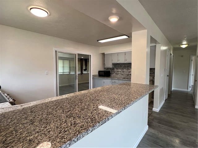 kitchen with dark stone countertops, dark hardwood / wood-style flooring, kitchen peninsula, and tasteful backsplash