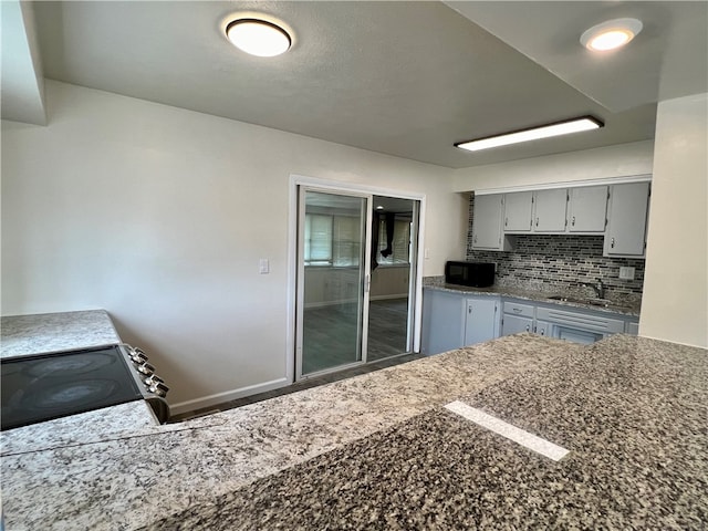 kitchen with dark stone countertops, backsplash, stove, sink, and gray cabinetry