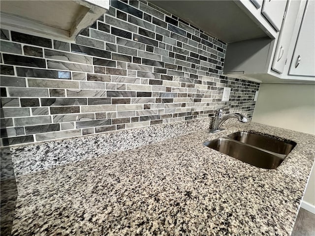 interior details with sink, white cabinets, tasteful backsplash, and light stone countertops