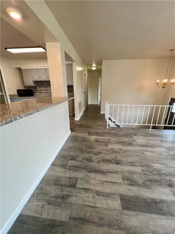 interior space featuring pendant lighting, light stone counters, decorative backsplash, white cabinetry, and dark wood-type flooring