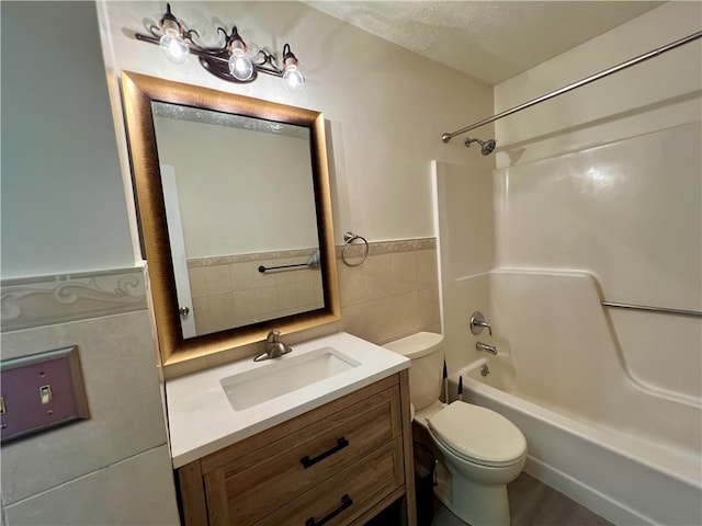 full bathroom with vanity, tile walls, washtub / shower combination, toilet, and a textured ceiling