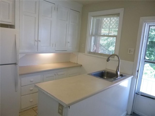 kitchen with light countertops, white cabinets, a sink, and freestanding refrigerator