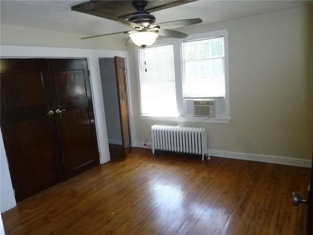 unfurnished bedroom featuring cooling unit, wood finished floors, baseboards, multiple closets, and radiator