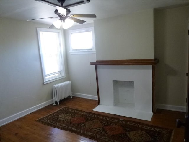 unfurnished living room featuring radiator heating unit, a fireplace with flush hearth, ceiling fan, wood finished floors, and baseboards