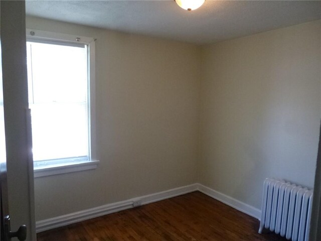 spare room with radiator, dark wood finished floors, and baseboards