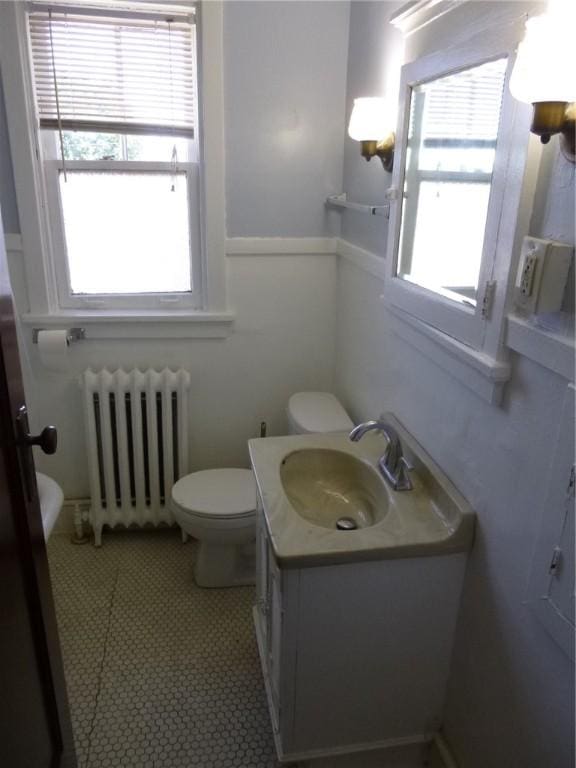 half bathroom with vanity, toilet, and radiator