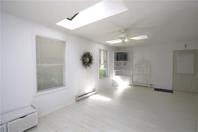 spare room featuring ceiling fan, baseboard heating, a skylight, and light hardwood / wood-style floors