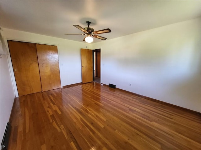 unfurnished bedroom with wood-type flooring, a baseboard heating unit, ceiling fan, and a closet