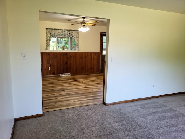 empty room featuring ceiling fan, wooden walls, and carpet flooring