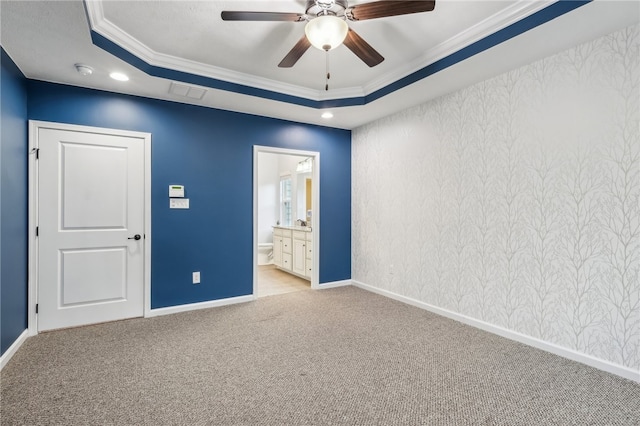 unfurnished bedroom with light colored carpet, ensuite bathroom, ceiling fan, and a tray ceiling