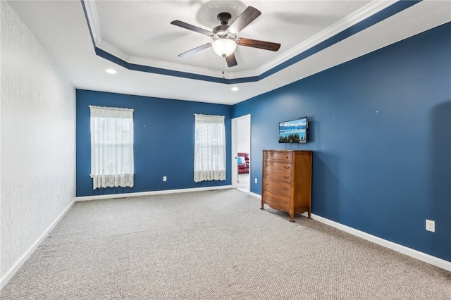 empty room with ornamental molding, carpet flooring, ceiling fan, and a tray ceiling