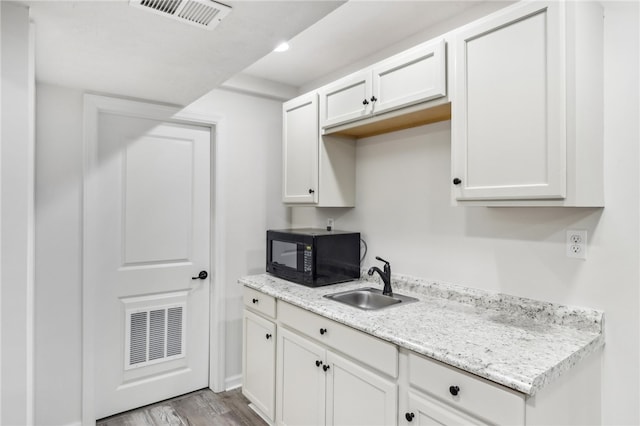 kitchen with sink, light stone countertops, light hardwood / wood-style flooring, and white cabinetry