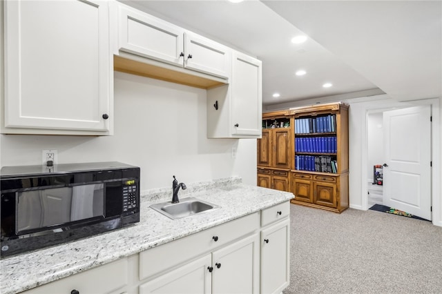 kitchen with white cabinets, light stone countertops, light colored carpet, and sink