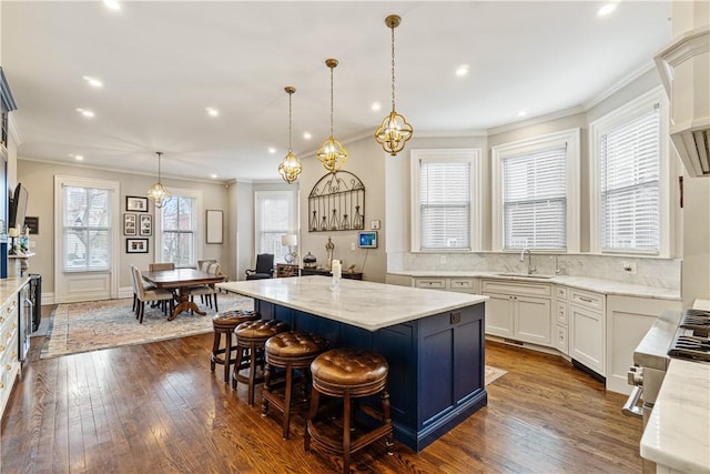 kitchen featuring a center island with sink, a kitchen bar, hanging light fixtures, dark wood-type flooring, and light stone counters