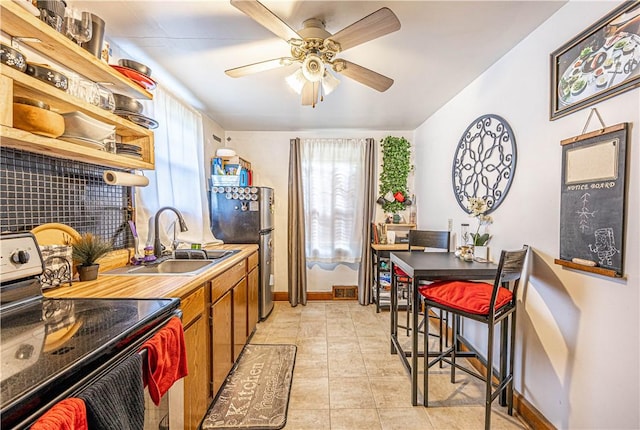 kitchen featuring light tile patterned flooring, ceiling fan, black range with electric cooktop, sink, and stainless steel refrigerator