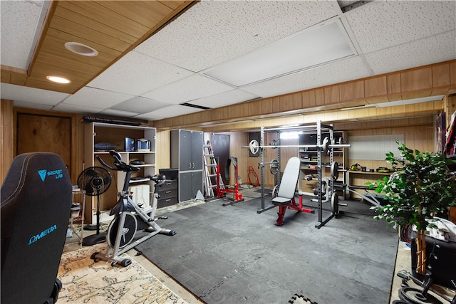 workout room featuring a paneled ceiling, wooden walls, and concrete floors