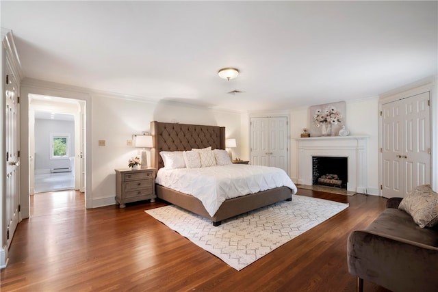 bedroom featuring multiple closets, dark wood-type flooring, and a baseboard heating unit