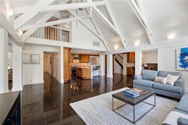 living room featuring decorative columns, beamed ceiling, dark tile patterned flooring, and high vaulted ceiling