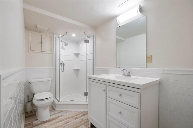 bathroom with vanity, hardwood / wood-style flooring, walk in shower, tile walls, and toilet