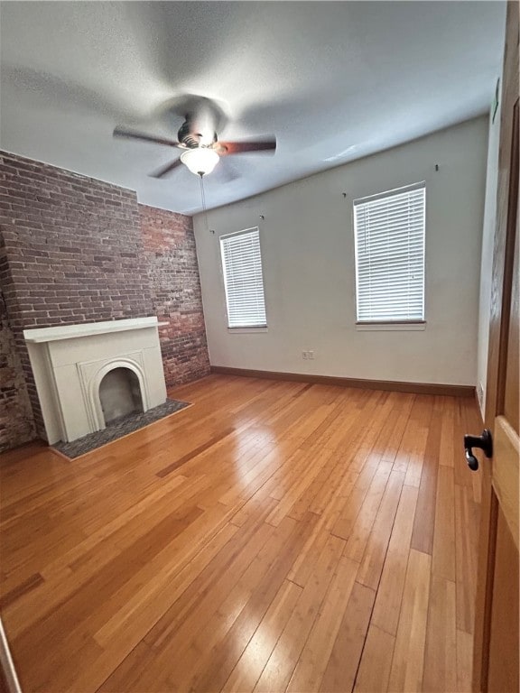 unfurnished living room with hardwood / wood-style flooring, a textured ceiling, brick wall, and ceiling fan