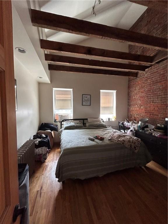 bedroom with beamed ceiling, wood-type flooring, and radiator heating unit