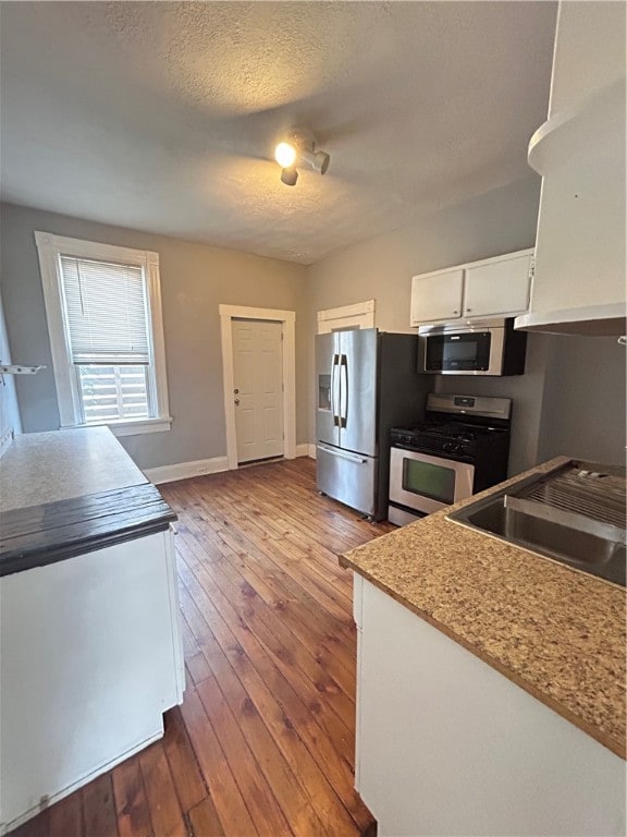 kitchen featuring white cabinets, light stone counters, appliances with stainless steel finishes, hardwood / wood-style flooring, and sink