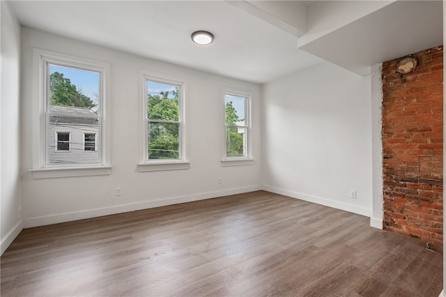 empty room featuring brick wall and hardwood / wood-style floors