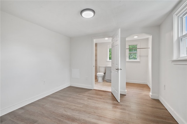 unfurnished bedroom with ensuite bathroom and light wood-type flooring