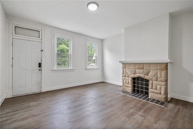 unfurnished living room featuring a stone fireplace and dark hardwood / wood-style floors