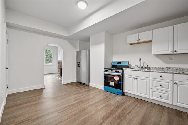 kitchen with white cabinets, light wood-type flooring, stainless steel fridge with ice dispenser, sink, and stove