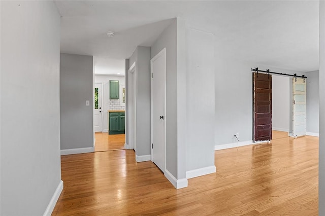 corridor with light wood-type flooring and a barn door