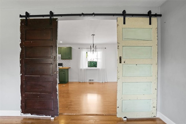 interior space with decorative light fixtures, a barn door, green cabinets, and wood-type flooring