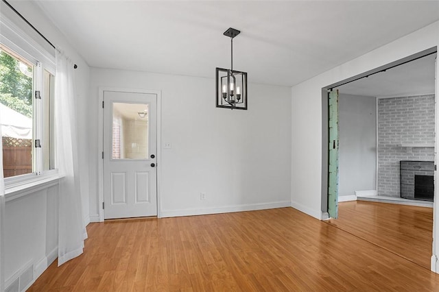 unfurnished dining area featuring light wood-type flooring, a notable chandelier, and a brick fireplace